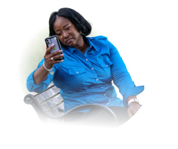 Una mujer sentada en un banco con la vista hacia la izquierda mira su teléfono celular. 